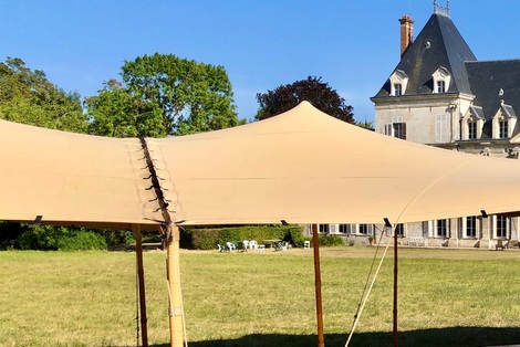 Grande tente nomade beige installée dans le parc d’un château, offrant un espace couvert élégant pour un événement extérieur.