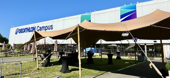 Tente nomade beige installée devant Decathlon Campus, aménagée avec des mange-debout pour accueillir un événement extérieur.