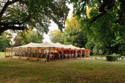 Tente nomade beige installée dans un parc arboré pour une réception de mariage conviviale, entourée d’un vaste jardin.