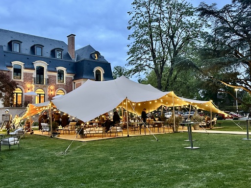 Tente nomade beige illuminée et aménagée pour une réception élégante en extérieur, dans le parc d’un château.