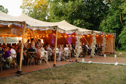 Réception de mariage sous une tente nomade beige décorée de guirlandes lumineuses et fleurs, avec invités à table.