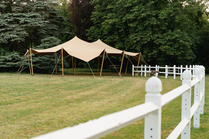 Tente nomade beige installée dans un vaste parc verdoyant, offrant un espace couvert élégant pour une réception de mariage.