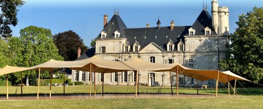 Tentes nomades beiges installées dans le parc d’un château, créant un vaste espace couvert pour des événements extérieurs.