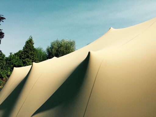 Toile tendue beige aux formes ondulées et élégantes, conçue pour créer un espace couvert lors d’événements en extérieur.
